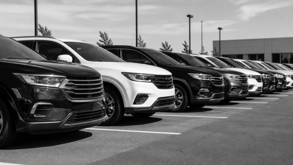 Row of modern cars parked in a dealership lot with clear sky.
