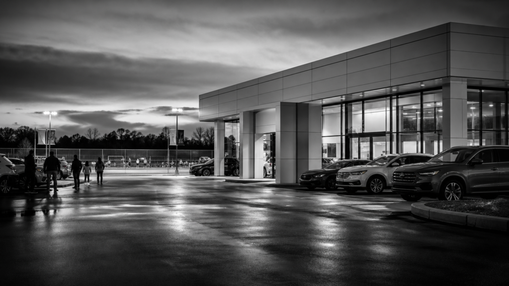 Modern car dealership building with parked cars and people outside at dusk.